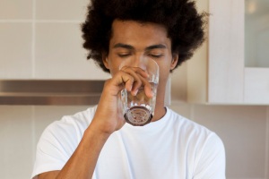 A young man drinking a glass of water in a kitchen