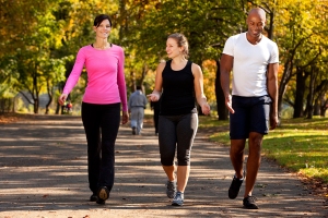 Two women and a man wearing athletic clothing and walking side by side in a park.