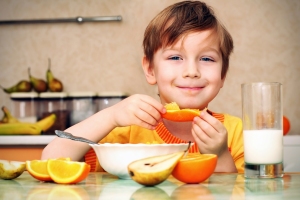 Young boy eating orange slices at the kitchen table.