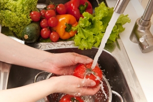 Close-up of a woman washing tomatoes in a colander in the sink.