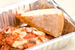 Lasagna and bread in an aluminum to-go container.
